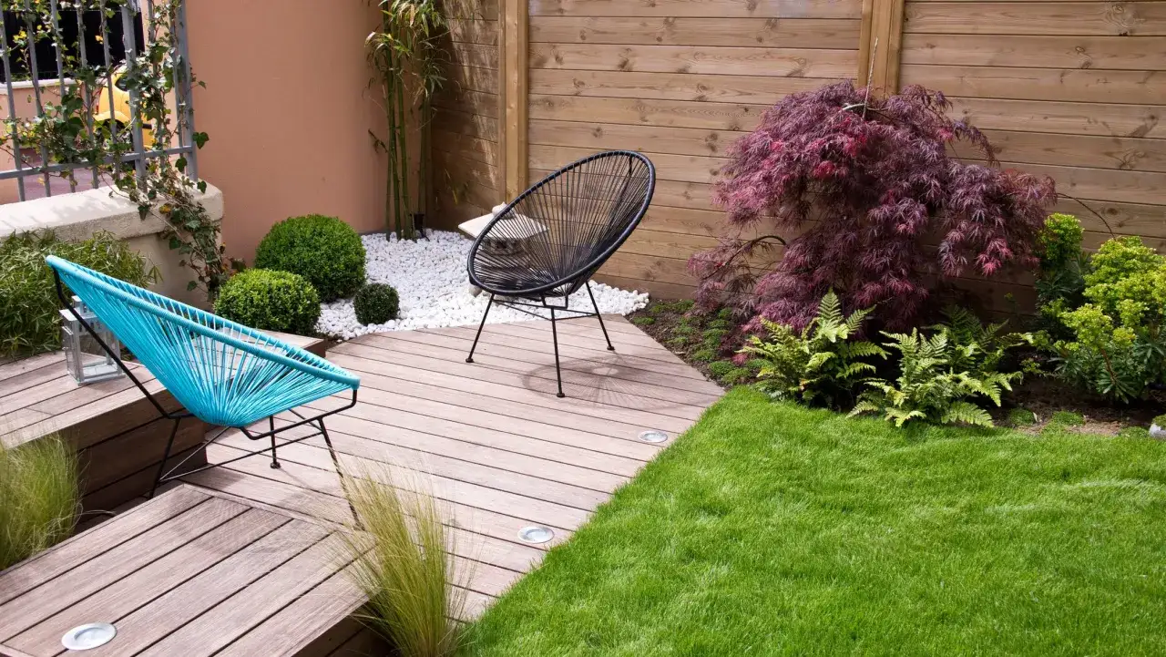 Dos sillas modernas en un patio con c&eacute;sped verde, plantas exuberantes y peque&ntilde;os jardines cuidados.