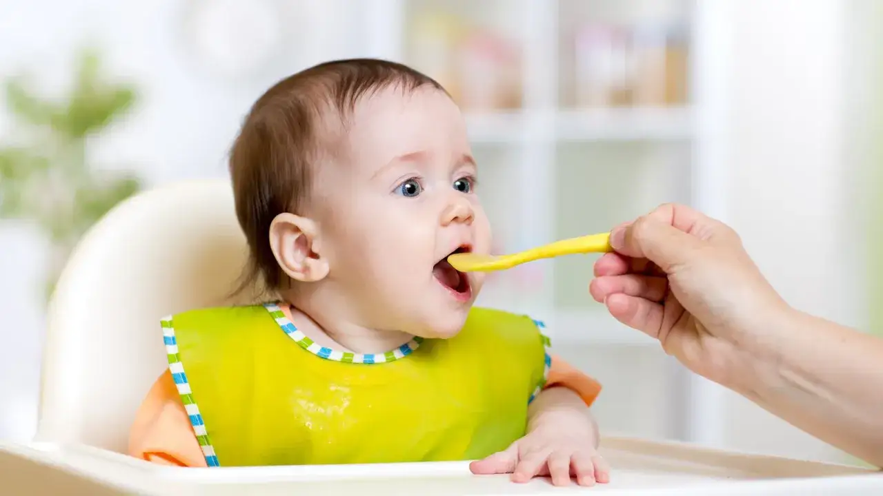 Ein Baby mit Lätzchen wird gefüttert. Die Augen sind weit geöffnet, ein Zeichen, dass es bereit ist für Brei. Reifezeichen Baby.