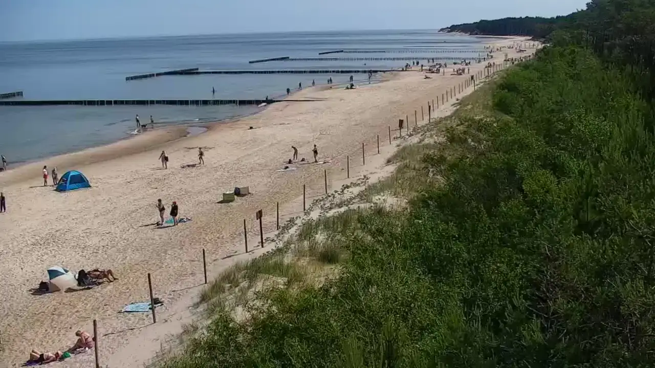 Plaża nad Bałtykiem, z ludźmi odpoczywającymi na piasku i w wodzie. Wygląda jak polski Dubaj nad morzem.