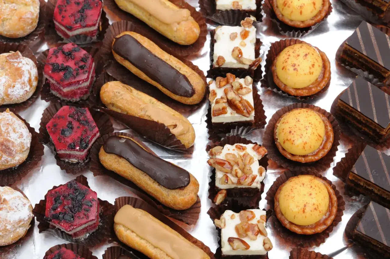 Variedad de petit four que es: &eacute;clairs de chocolate y caramelo, pastelitos de frutos rojos, cuadrados de crema con nueces, tartas de crema amarilla y pastelitos de chocolate.