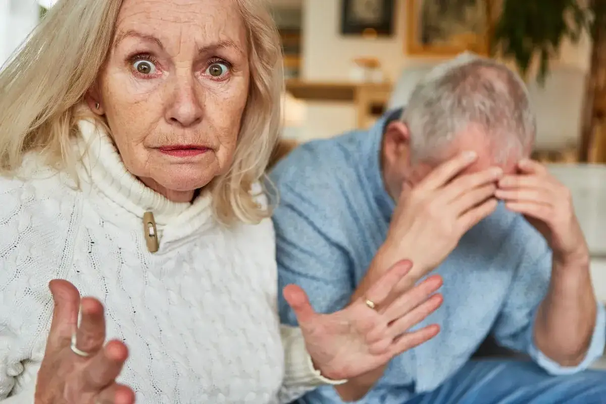 Zmartwiona seniorka gestykuluje, podczas gdy jej partner ukrywa twarz w dłoniach. Problemy ze snem i brak apetytu u seniora mogą być powodem ich zmartwienia.