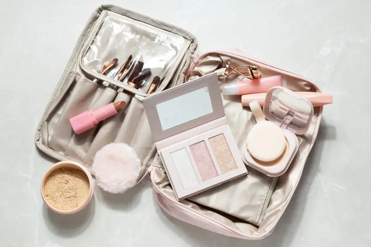 Une trousse de maquillage bagage cabine ouverte, r&eacute;v&eacute;lant pinceaux, rouge &agrave; l&egrave;vres, palette d'highlighters, poudre et gloss.