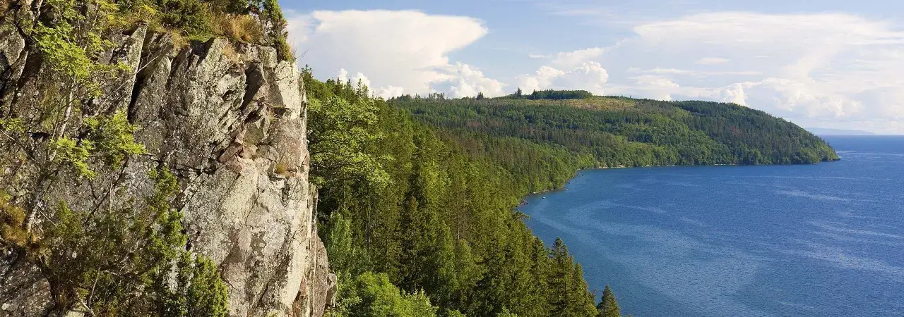 En dramatisk klippv&auml;gg m&ouml;ter en djupbl&aring; sj&ouml;, kantad av t&auml;ta skogar. Perfekt f&ouml;r en omberg vandring med hisnande vyer.