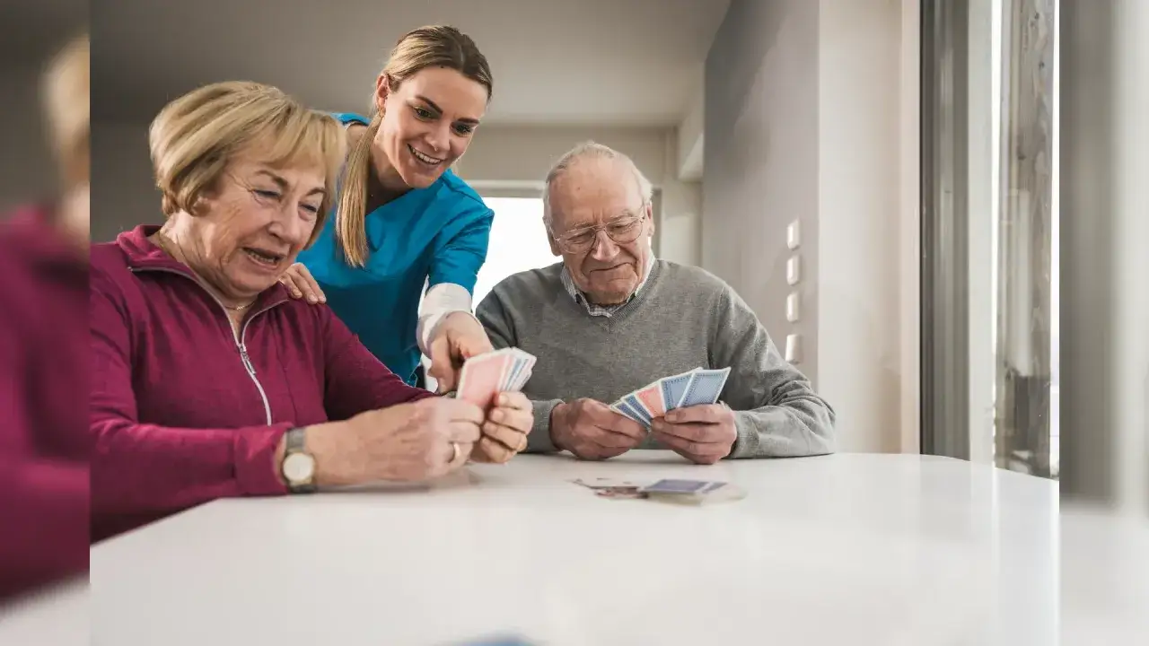 Une aide-soignante encourage des personnes &acirc;g&eacute;es &agrave; jouer aux cartes, stimulant ainsi leurs exercices orthophoniques et leur m&eacute;moire.