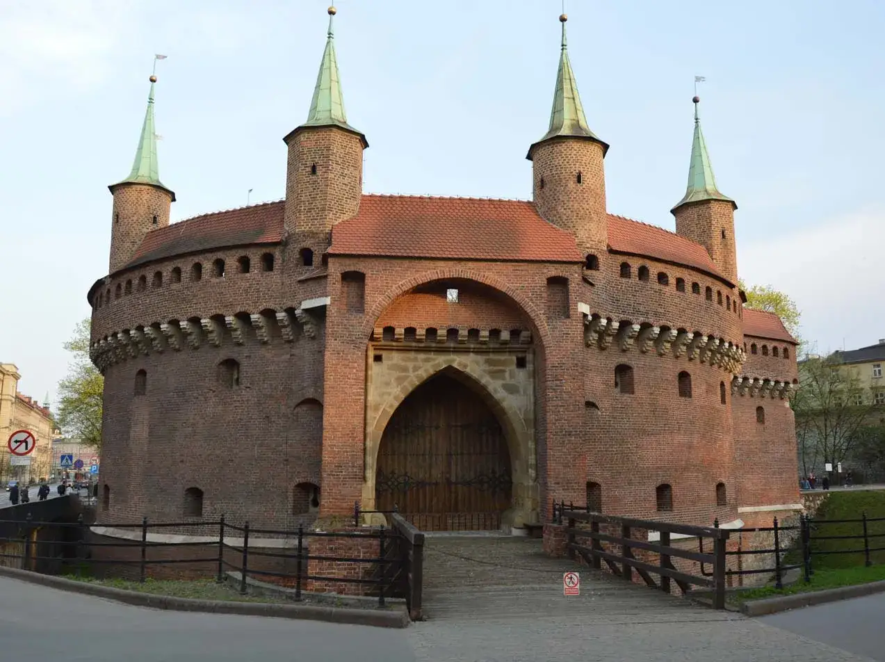 Imponujący barbakan kraków z drewnianym mostem i zielonymi wieżyczkami.