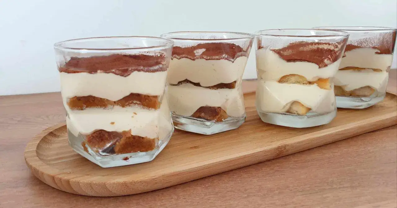 Quatre verrines de tiramisu maison, superposant biscuits &agrave; la cuill&egrave;re imbib&eacute;s et cr&egrave;me onctueuse, saupoudr&eacute;es de cacao.