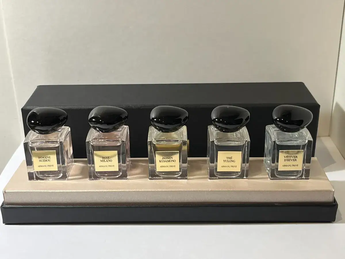 Pięć flakonów perfum Armani Prive z czarnymi, błyszczącymi nakrętkami, ustawionych na eleganckiej podstawce.