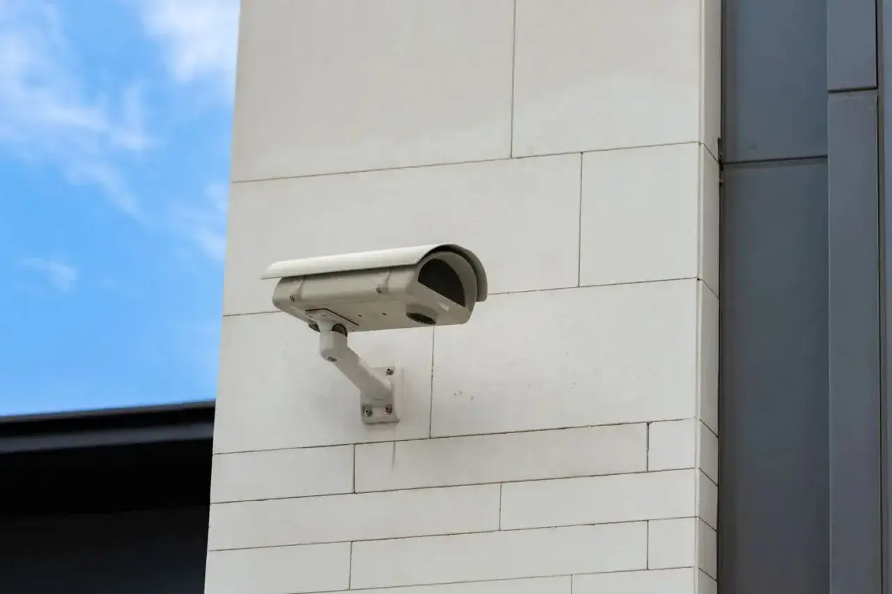 Caméra de surveillance fixée sur un mur blanc, prête à filmer. On peut imaginer quelqu'un cherchant à empêcher une caméra de filmer.
