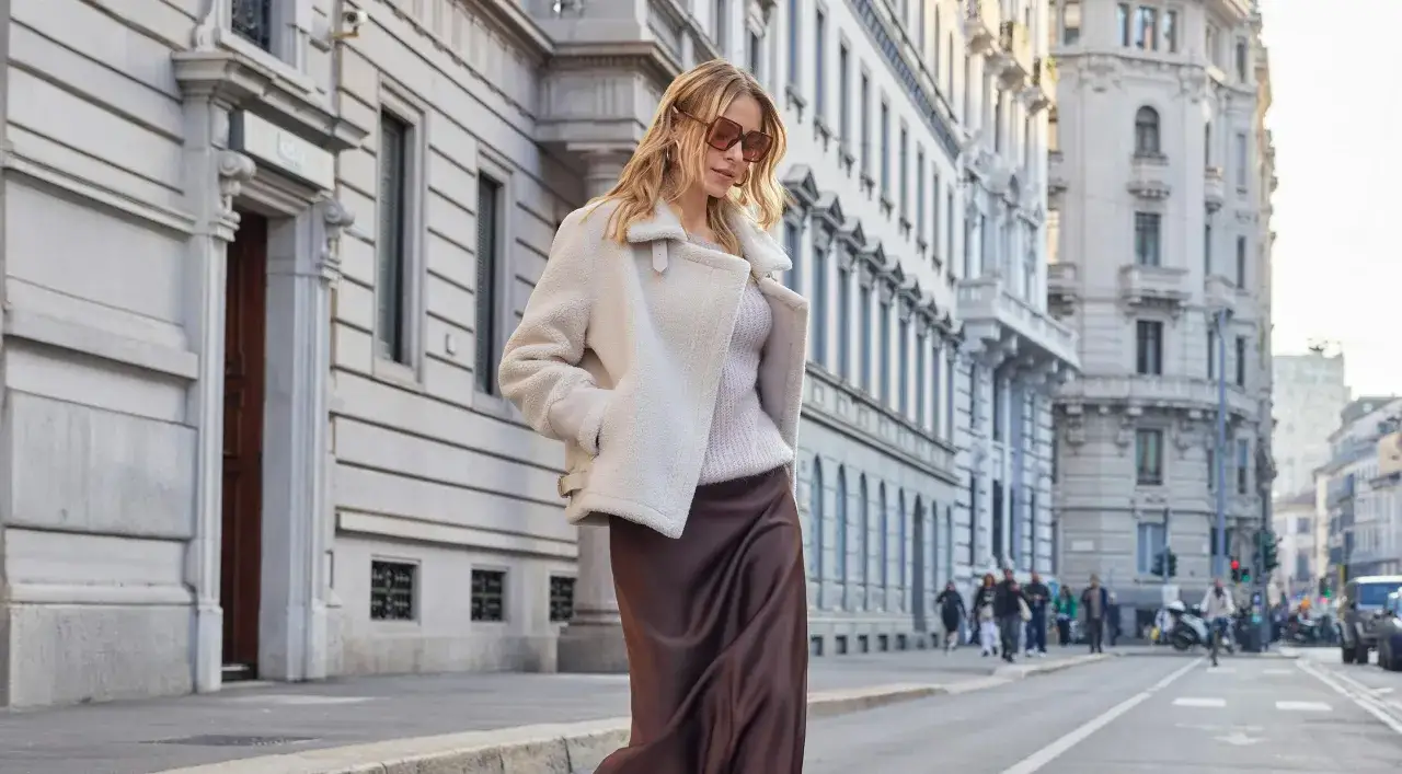 Donna con cappotto bianco teddy e gonna di seta marrone cammina in citt&agrave;. Il capispalla significato &egrave; eleganza e comfort.