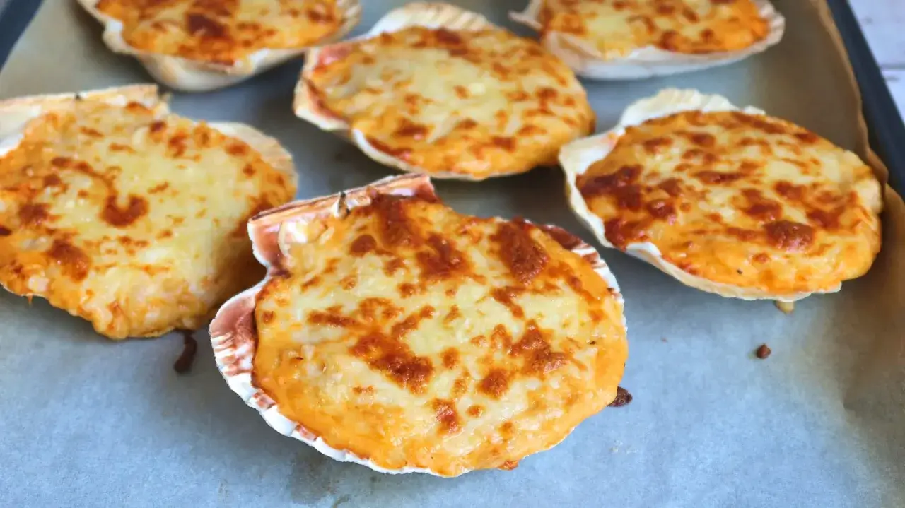 Vieiras gratinadas con queso dorado y burbujeante, listas para ser disfrutadas.