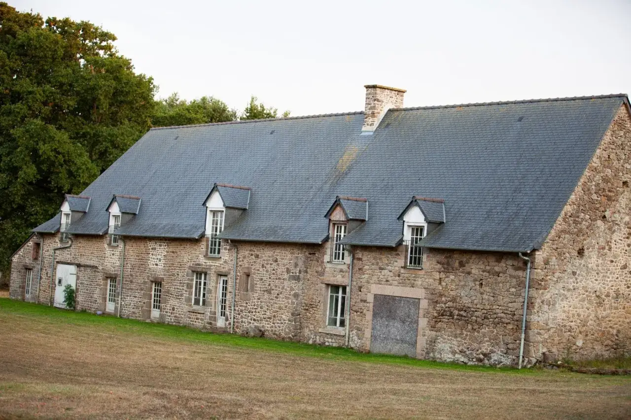 Longère en pierre avec toit d'ardoise, projet d'aménagement en cours. Fenêtres à petits carreaux, cheminée en pierre.