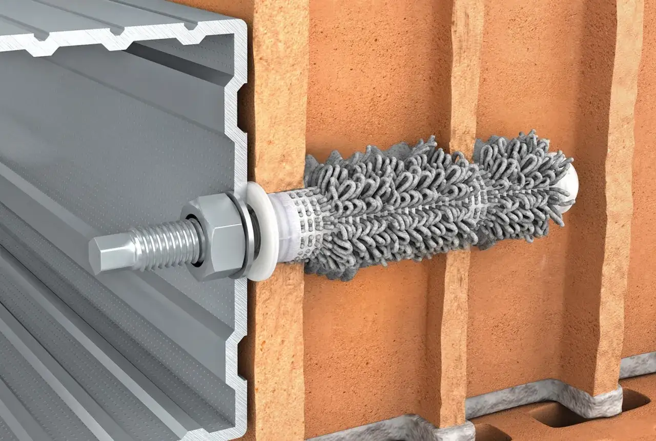 Przekrój przez cegłę z widocznym systemem kotwienia: śruba z nakrętką mocuje profil aluminiowy do ściany, gdzie kotwy chemiczne zapewniają stabilne połączenie.