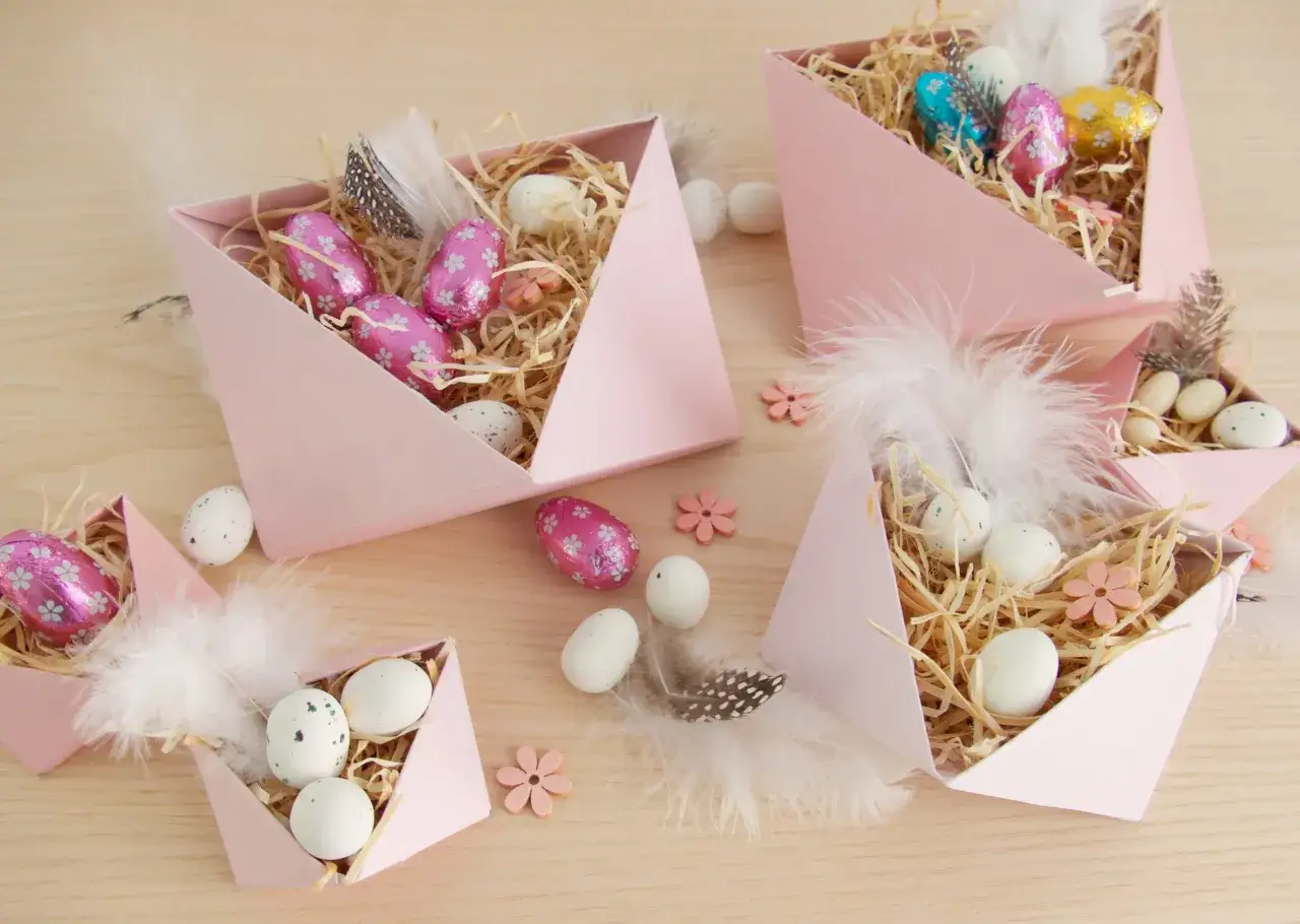 DIY Osternest-Ideen: Rosa Schachteln gefüllt mit Stroh, bunten Schokoladen- und echten Eiern, Federn und kleinen Holzblumen.