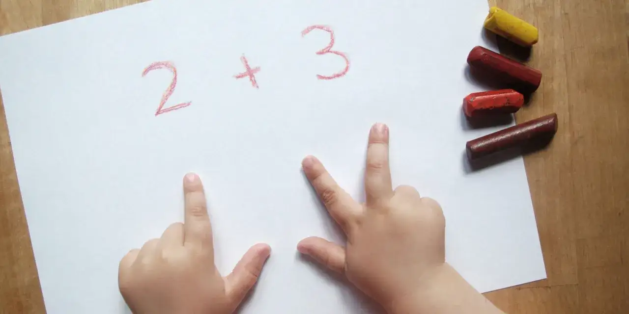 Kinderh&auml;nde zeigen die Kraft der 5 beim Rechnen: 2 + 3. Buntstifte liegen bereit.
