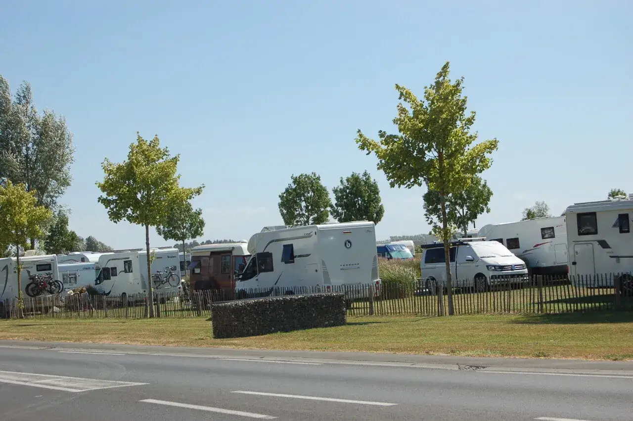 Aire de camping-car près du Mont Saint-Michel. Plusieurs camping-cars blancs sont garés sur un terrain herbeux, sous un ciel bleu clair.