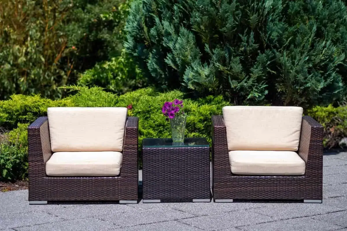 Dos sillones y mesa auxiliar de rattan oscuro con cojines beige, perfectos para el mantenimiento de muebles de rattan en exteriores.