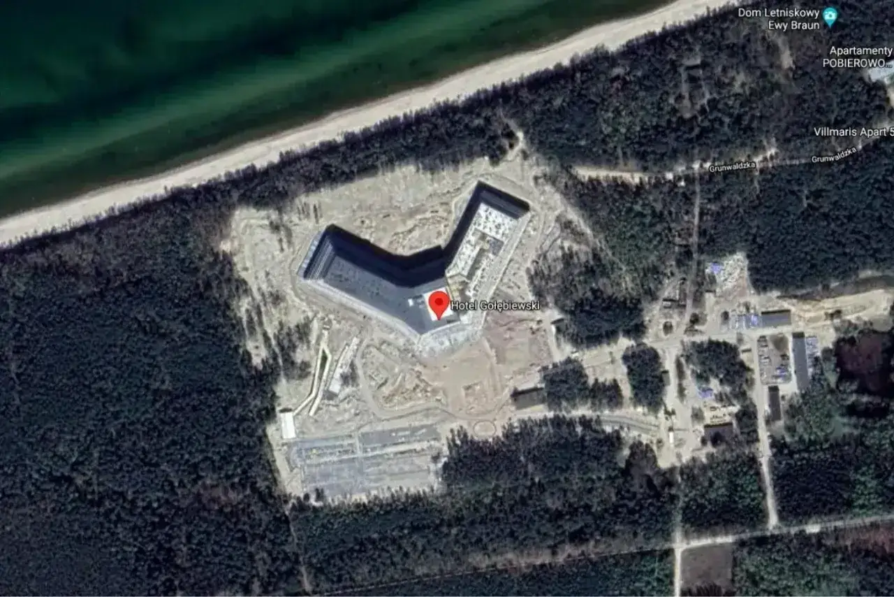 Widok z lotu ptaka na budowę hotelu Gołębiewski w Pobierowie. Obiekt w kształcie litery V powstaje blisko plaży, otoczony lasem.