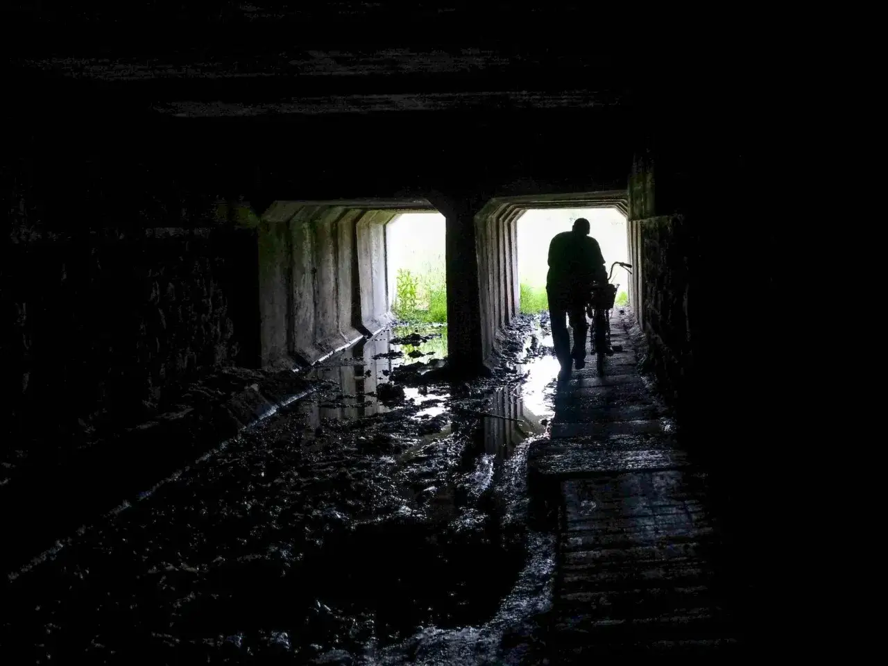 Mroczny tunel, błoto i woda. Postać z rowerem wychodzi na światło, jakby uciekała z najbardziej nawiedzonego miejsca w Polsce.