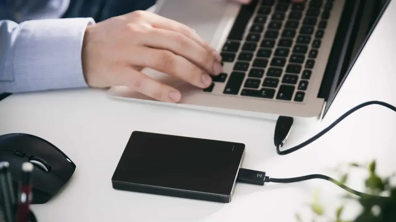 Persona trabajando en portátil, con ratón y disco duro externo conectado. El sistema no detecta disco duro externo.