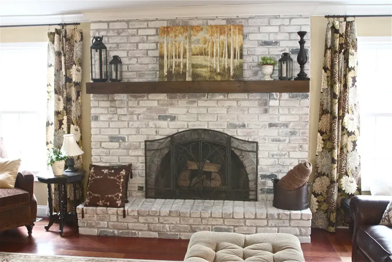 A rustic fireplace with whitewashed brick, a wooden mantel, and a decorative screen. This image shows how to whitewash brick for a charming, updated look.