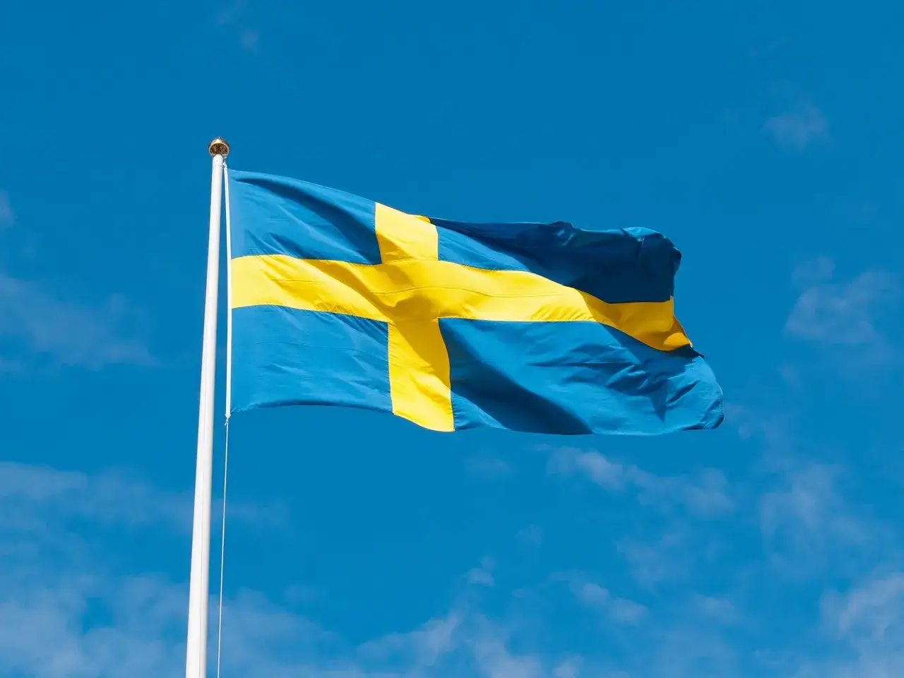 Svenska flaggan historia: Blå och gul korsflagga vajar stolt mot en klarblå himmel.