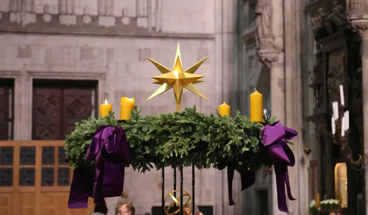 Ein Adventskranz mit vier gelben Kerzen und einem goldenen Stern, geschmückt mit lila Bändern. So wird die besinnliche Zeit vor Weihnachten, das advent, gefeiert.