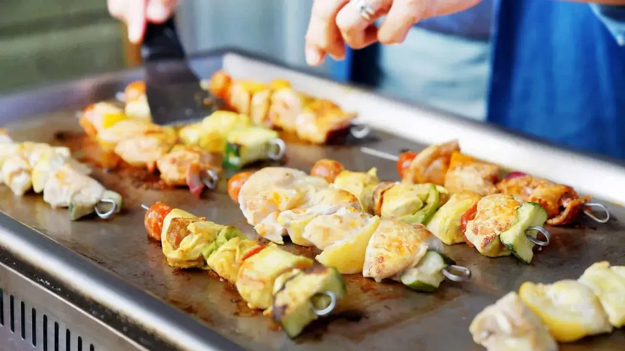 Brochettes de poulet et l&eacute;gumes grillant sur une plancha. Une excellente recette plancha pour un repas estival.