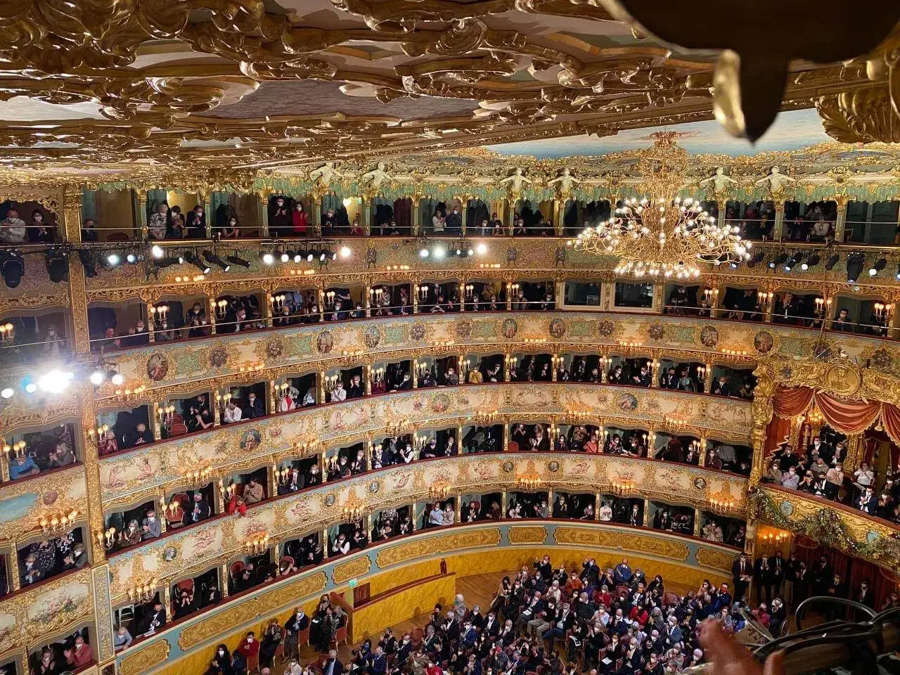 Interno dorato del Teatro La Fenice, con pubblico in platea e nei palchi. Il prezzo dei biglietti varia per la vista.