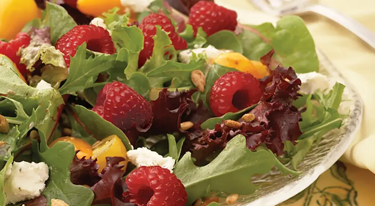 Frischer Salat mit Himbeeren, Ziegenkäse und Pinienkernen, beträufelt mit Himbeer-Vinaigrette.