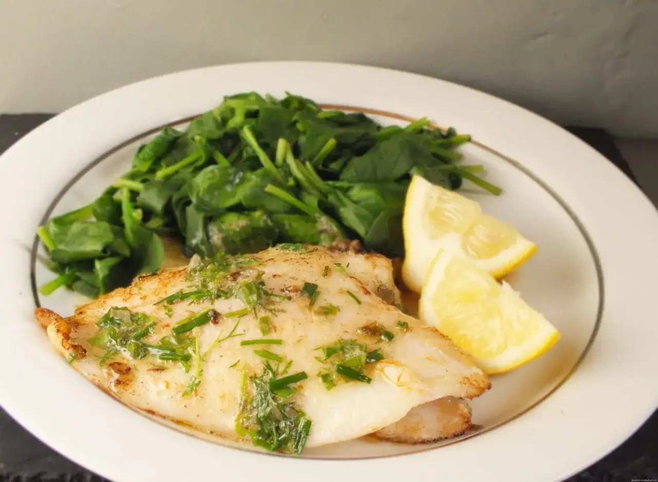 Filet de sole grillé, nappé d'herbes fraîches, servi avec des épinards et des quartiers de citron.