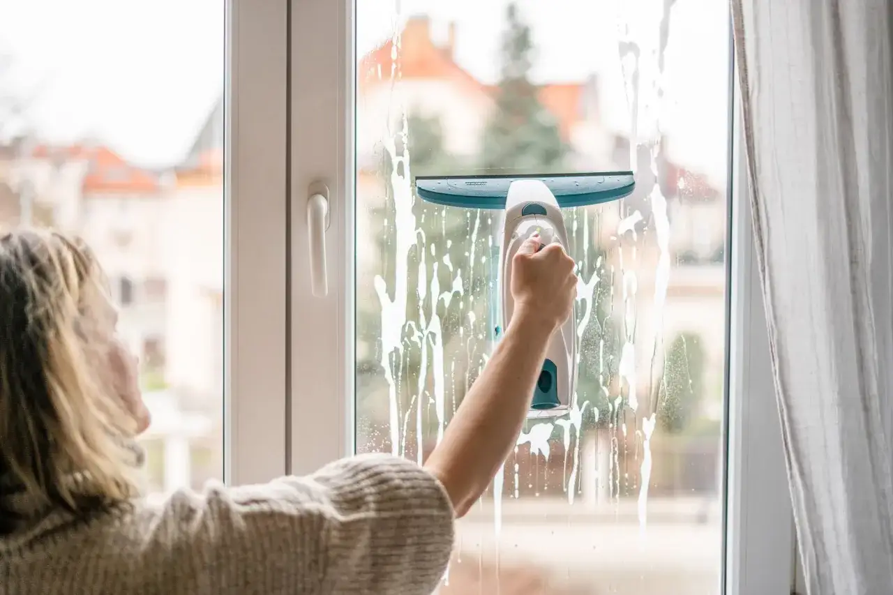 Kobieta myje okno elektryczną myjką, usuwając ślady po tynkowaniu.