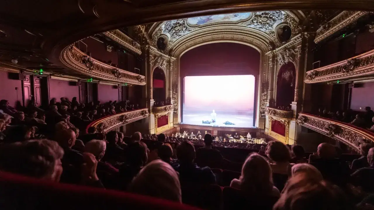 Publik njuter av en föreställning på en opera i Stockholm. En scen med en ensam figur och en orkester syns på scenen.