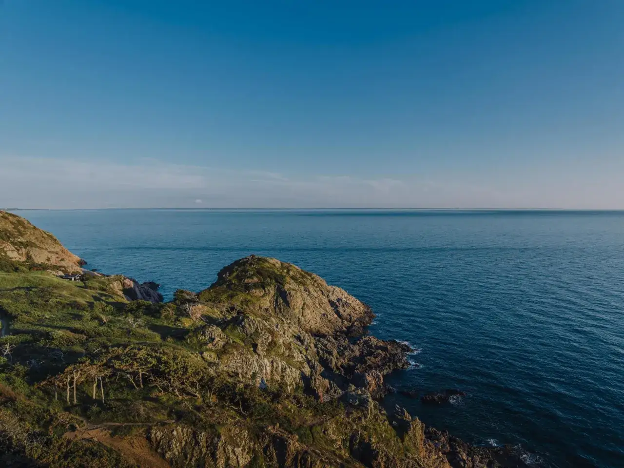 Klippor och grönska möter havet vid en vacker solnedgång i Skåne. En ensam stuga anas på sluttningen.