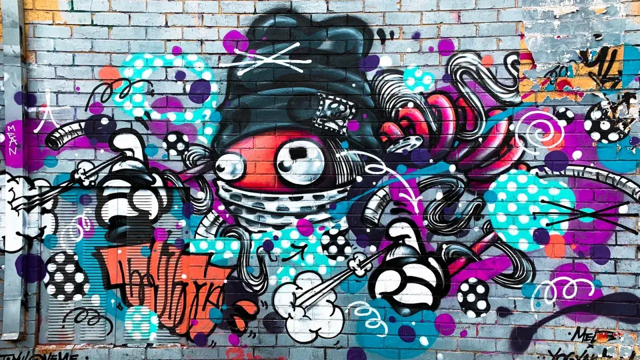 Färgglad graffiti på en tegelvägg med en stor, röd figur med stora ögon och en svart hatt. Konstnären har valt att måla graffiti med livliga färger och former.