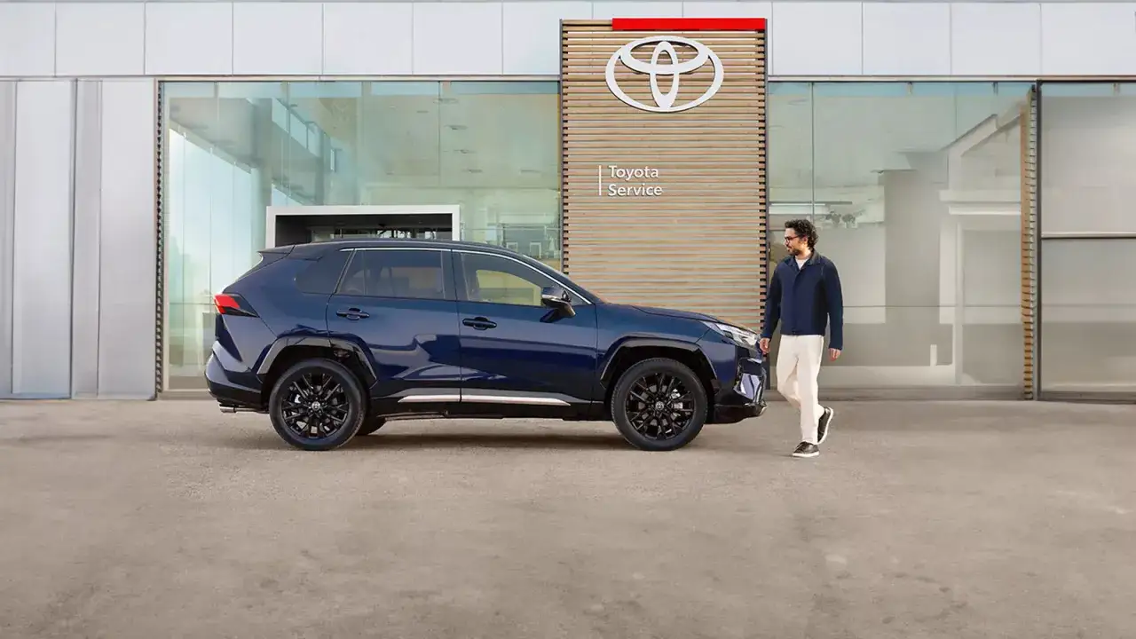 Mężczyzna idzie obok swojego nowego, granatowego SUV-a Toyoty przed salonem. To idealny moment na pierwszy przegląd gwarancyjny nowego samochodu Toyota.