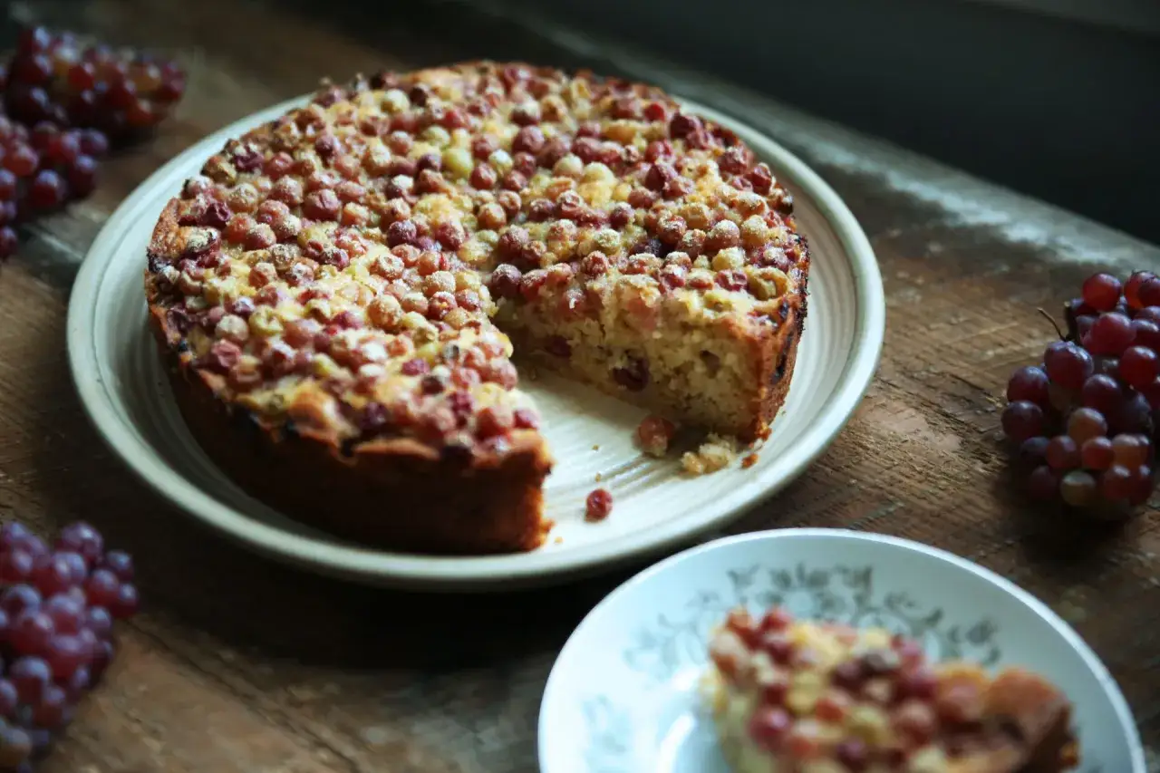 G&acirc;teau aux raisins secs moelleux, garni de fruits rouges. Une tranche est servie sur une assiette.