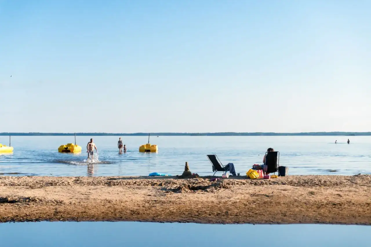 Solig dag vid Karlstad Swecamp Bomstadbaden. Folk badar och njuter av solen p&aring; stranden.