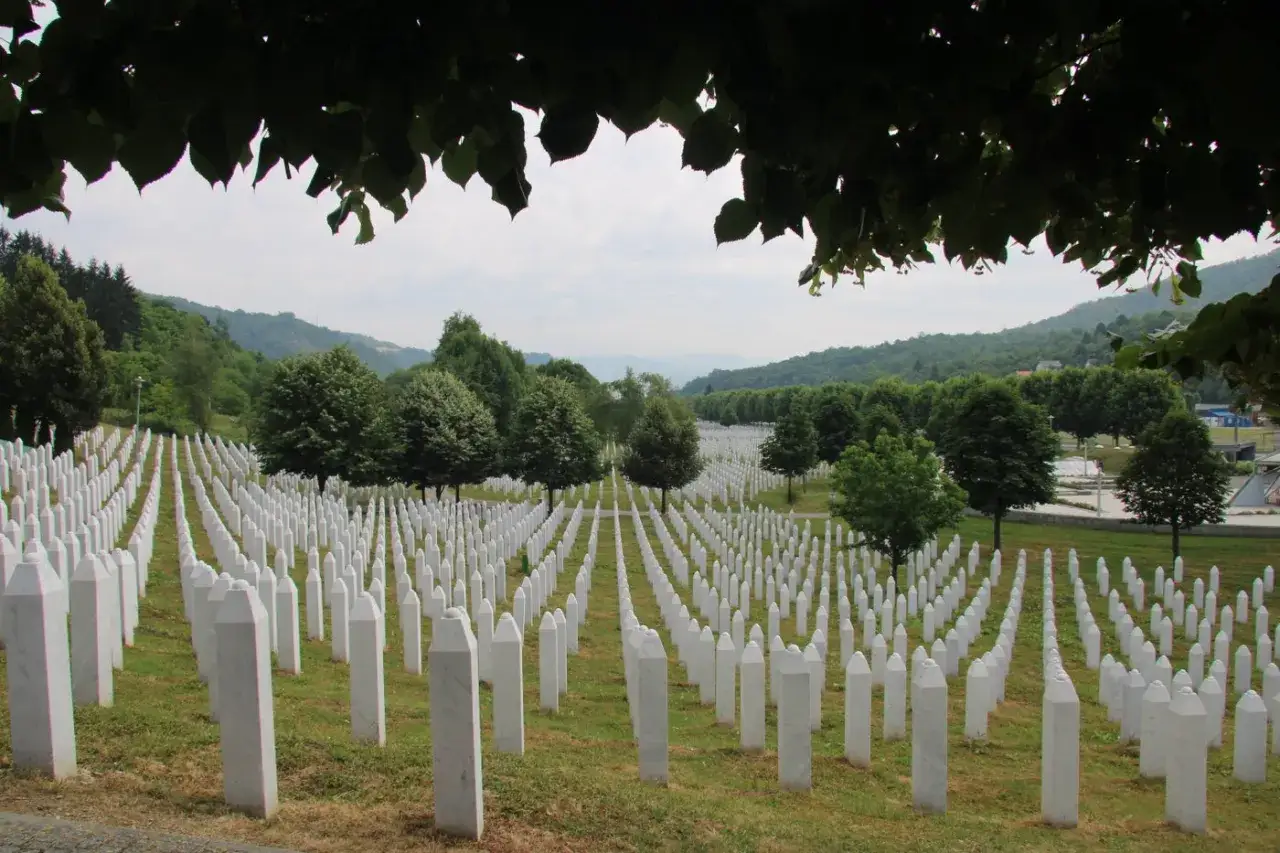 Enormt fält med vita gravstenar, en påminnelse om folkmordet i Srebrenica. Grönskande kullar i bakgrunden.