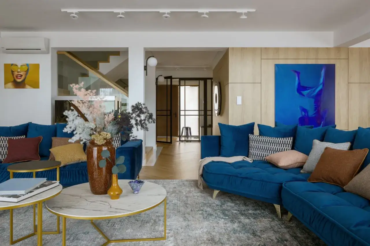Nowoczesny salon w stylu klasycznym wnętrza. Duża, granatowa sofa, marmurowe stoliki i drewniane panele tworzą elegancką przestrzeń.