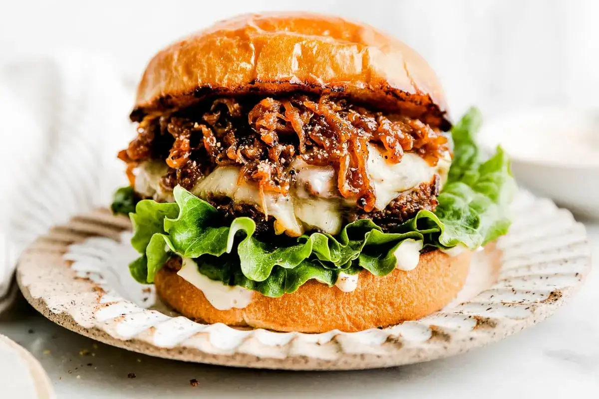 Saftiger Burger mit geschmolzenem Käse, knackigem Salat und karamellisierten Portwein Zwiebeln auf einem rustikalen Teller.
