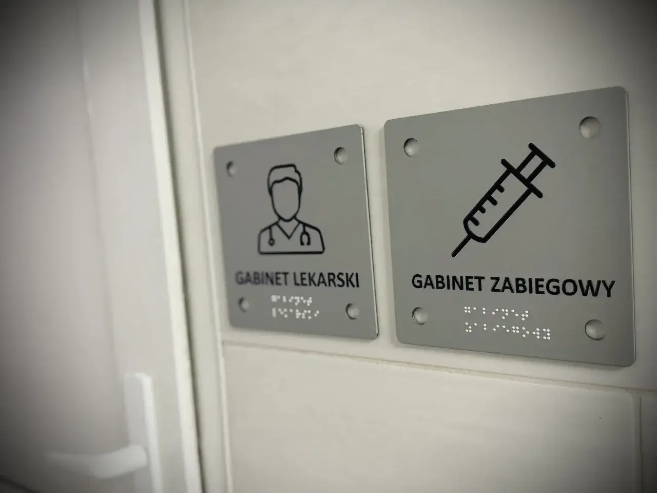 Tabliczki z piktogramami lekarza i strzykawki. Jedna z nich informuje o gabinecie lekarskim, gdzie przyjmuje felczer, druga o gabinecie zabiegowym.