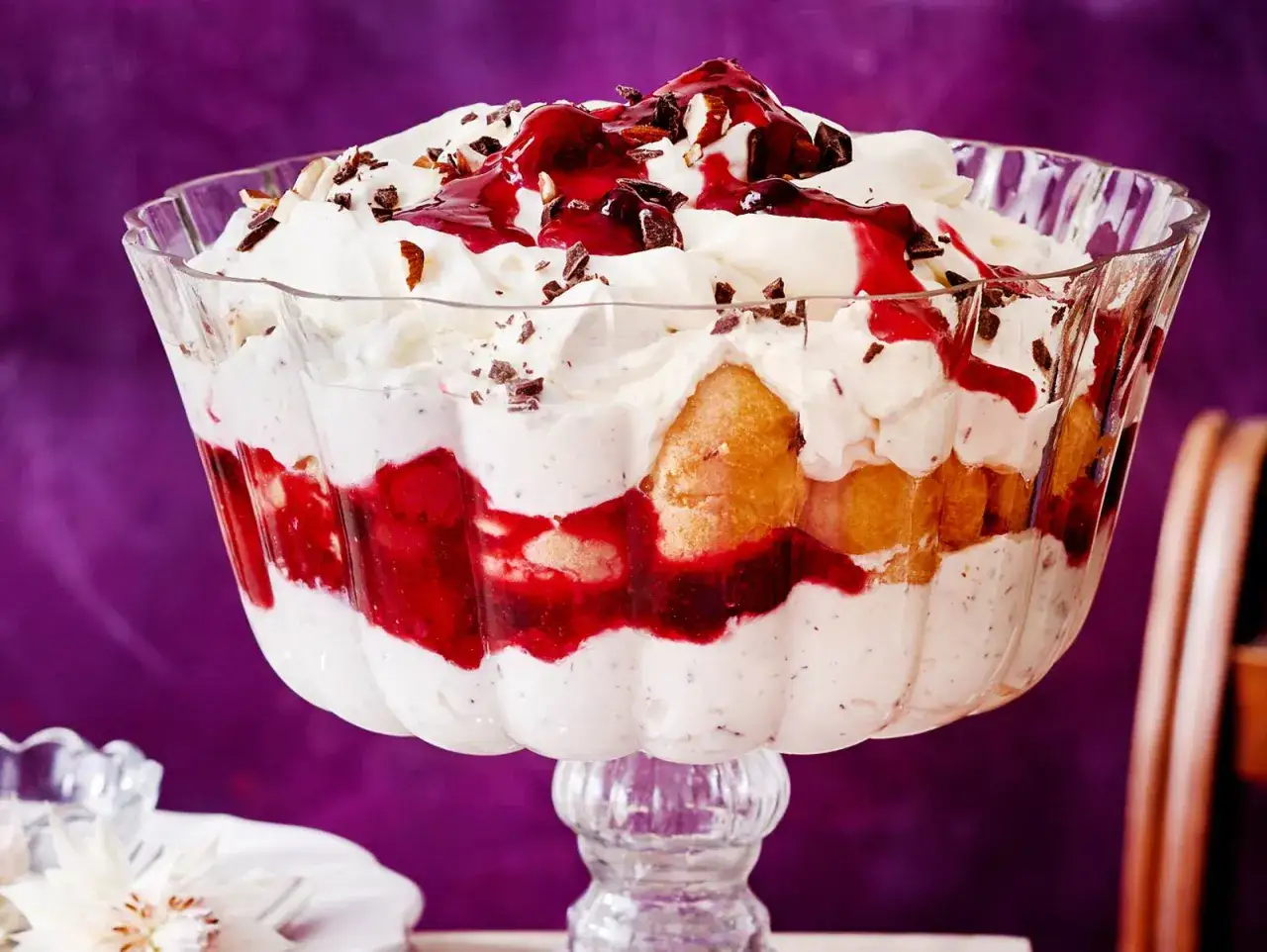 Ein &uuml;ppiges Windbeutel-Dessert in einer Glasschale, geschichtet mit Sahne, Kirschen und Biskuit, garniert mit Schokostreuseln und Mandeln.