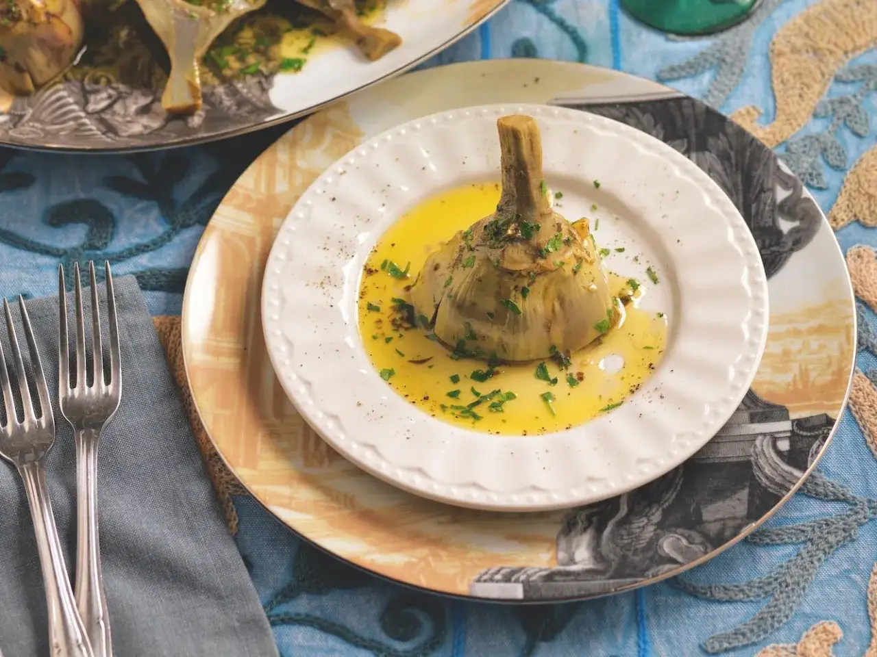 Un carciofo alla romana, tenero e profumato, servito su un piatto bianco con olio e prezzemolo.
