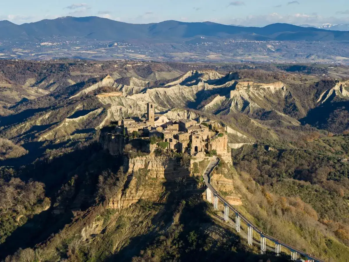 Civita di Bagnoregio, un borgo arroccato su un colle di tufo, domina un paesaggio di calanchi lunari. Un ponte pedonale collega il paese al mondo.