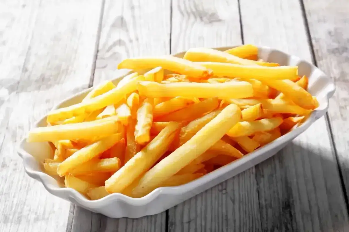 Złociste, chrupiące frytki McDonald's w białym opakowaniu, ułożone na drewnianym blacie.