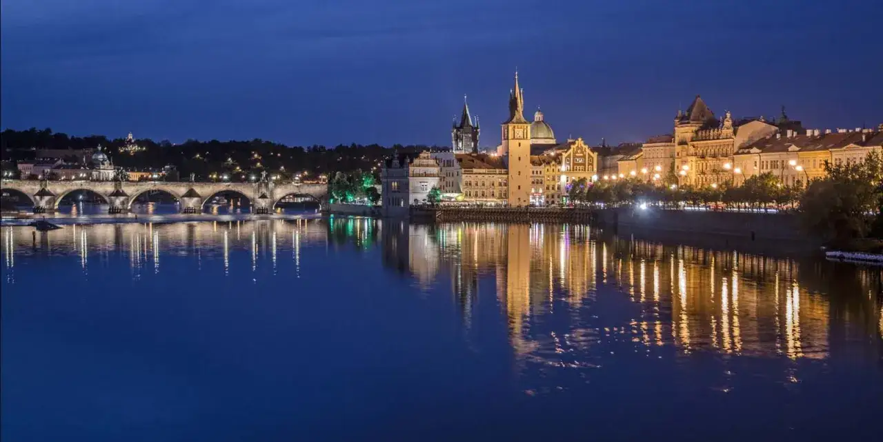 Nocne praga zwiedzanie: Most Karola i zabytkowe kamienice odbijające się w Wełtawie.