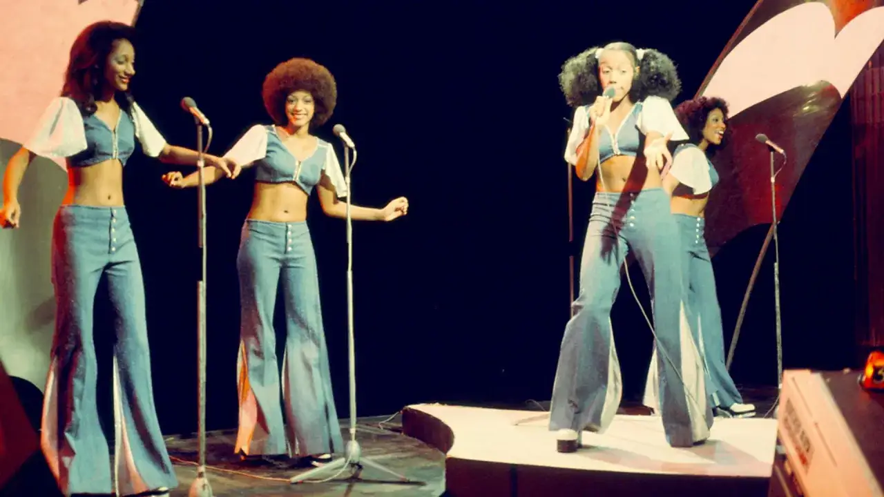 Quatre femmes chantent sur scène, vêtues de tenues disco évasées. L'ambiance est électrique, le disco bat son plein !