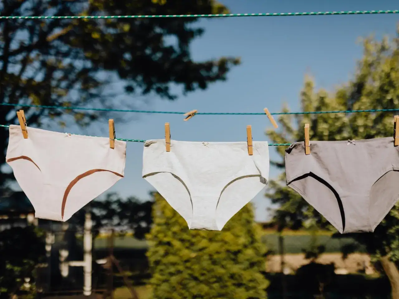 Drei Unterhosen in verschiedenen Grautönen trocknen an einer Wäscheleine. Ein Zeichen für frisch gewaschene Unterhosen im Freien.