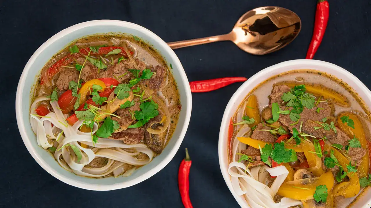 Dwie miski aromatycznej zupy z makaronem ryżowym, wołowiną, papryką i kolendrą, ozdobione papryczkami chili.