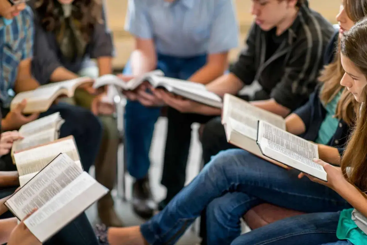 A diverse group of young people engage in a lively discussion, exploring various bible study topics from open books.